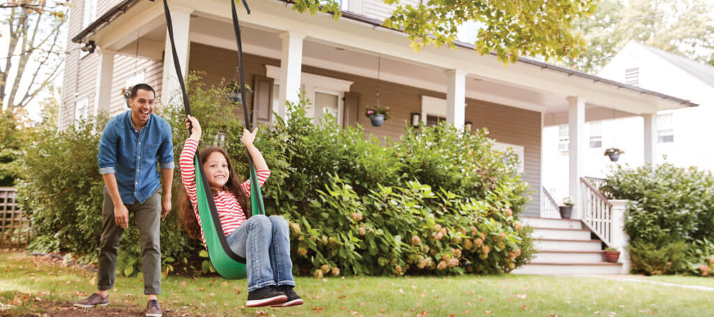 father pushing daughter on swing outside their home